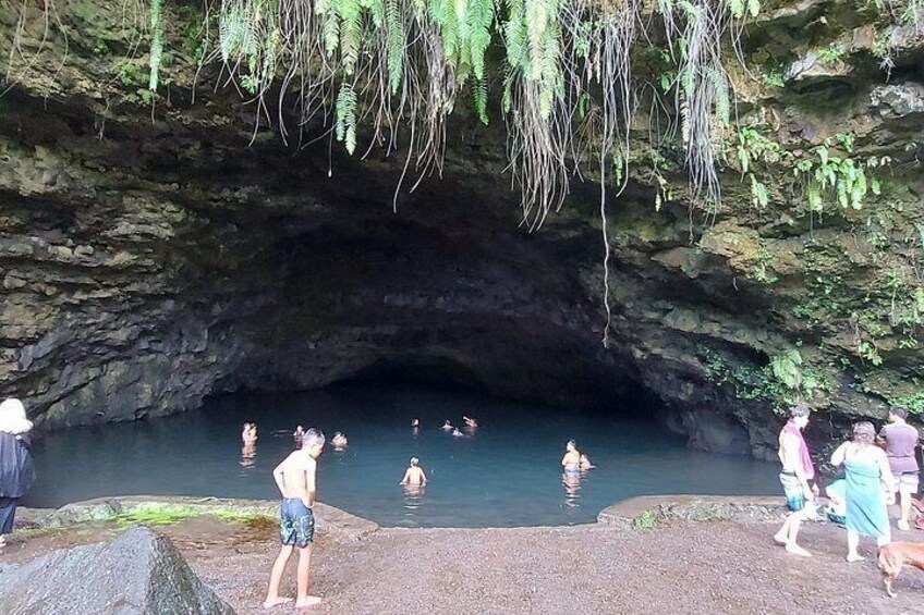 A natural cave entrance with people swimming in a pool of water. 3
