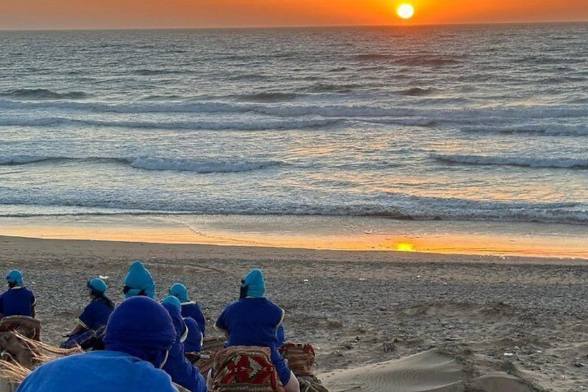 A sunset over the ocean with people sitting on the beach. 4