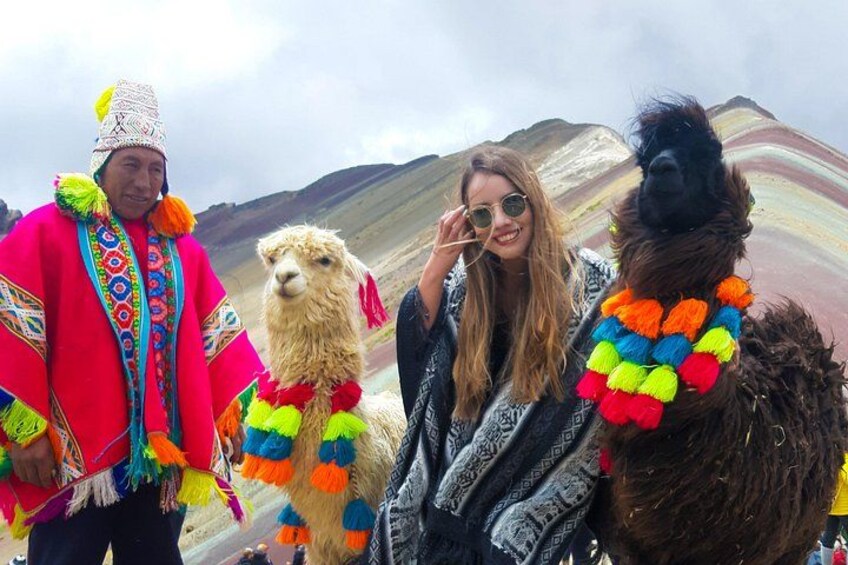 Une personne vêtue d’un costume traditionnel, accompagnée de lamas, dont l’un est décoré de motifs colorés, dans un paysage montagneux. 4