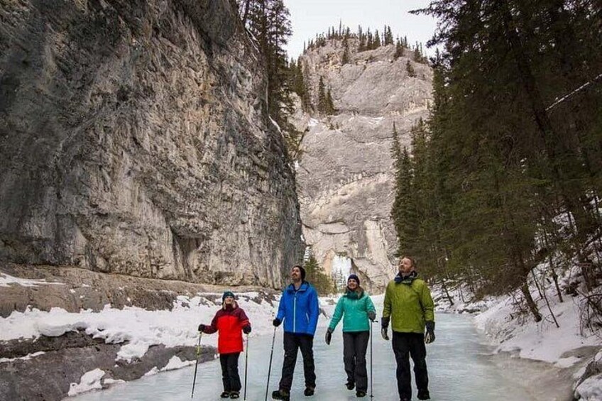Quatre personnes pratiquent le ski de fond sur une rivière bordée de falaises rocheuses et d’arbres. 1