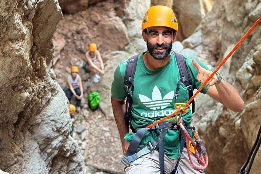 A person rappelling down a rocky cliff with a harness and helmet, surrounded by other climbers. 5
