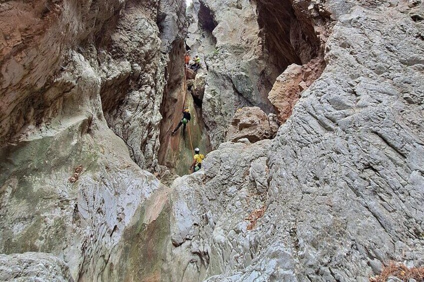A canyon with a narrow passage and a person rappelling down a rocky wall. 2