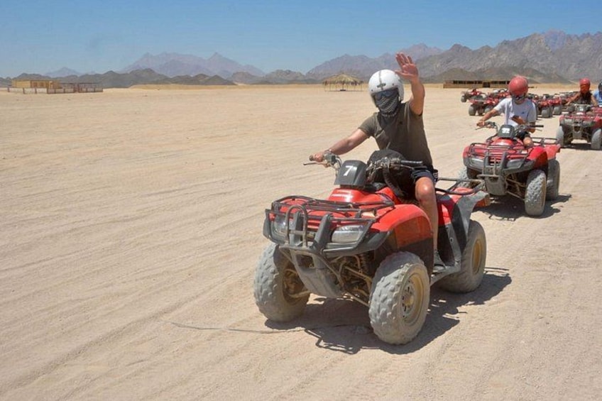 A person riding an ATV in a desert with mountains in the background. 2
