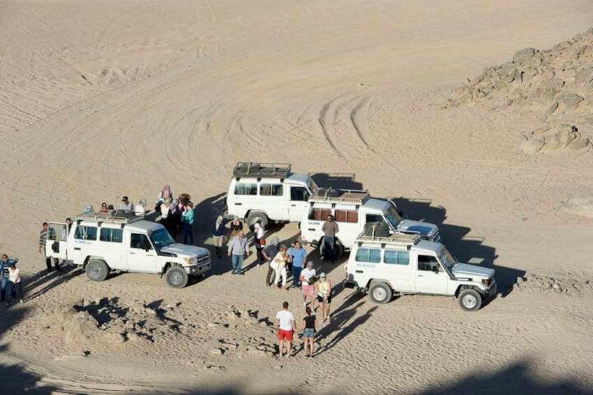 A group of white vehicles parked in a desert with people standing around them. 4