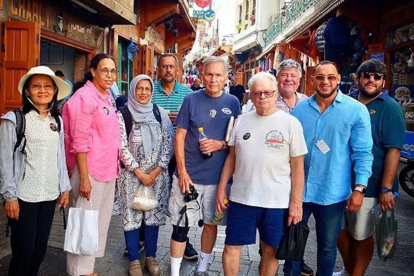 Un grupo de personas de pie en una calle con tiendas y edificios al fondo. 1