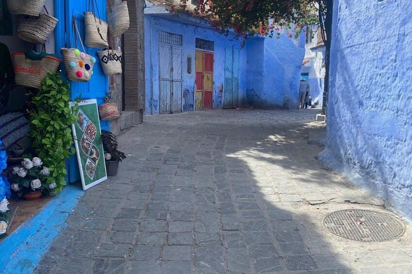 Una estrecha calle adoquinada con paredes pintadas de azul, cestas colgando a la izquierda, y un hombre caminando a lo lejos. 4