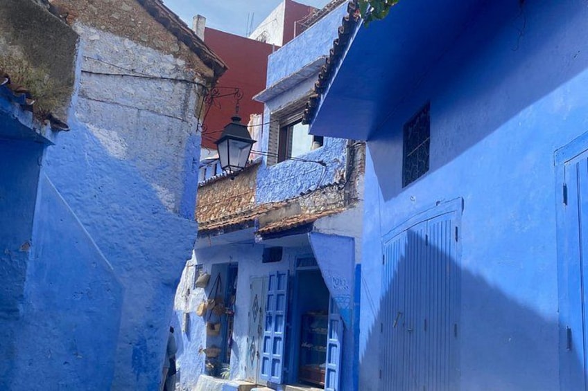 Un callejón estrecho con edificios pintados de azul, una puerta blanca y un techo rojo. 5