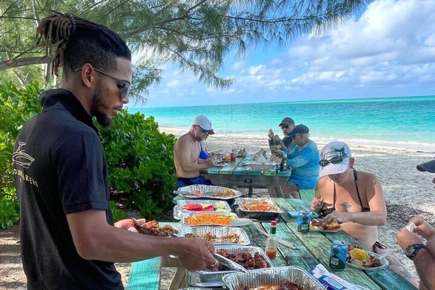 A group of people at a beach barbecue with food and drinks on a table. 2