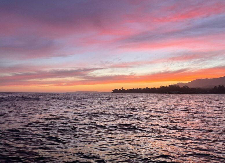 A sunset over a body of water with a silhouette of a coastline and mountains in the distance. 4