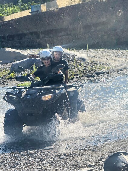 Two people on an ATV driving through a shallow water body. 2