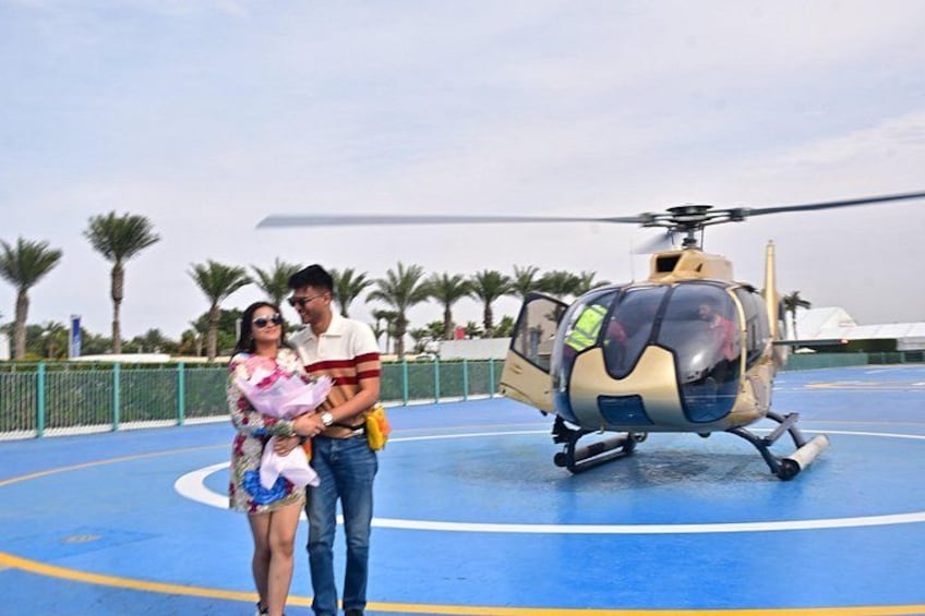 A couple standing on a blue surface with a helicopter in the background. 2