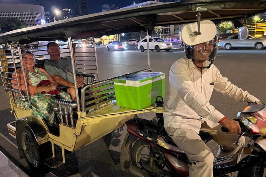 En motorcykel med en sidovagn som transporterar två passagerare, en grön container och en förare med hjälm. 4