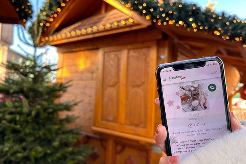 A smartphone displaying a Christmas tour app with a wooden building and a decorated Christmas tree in the background. 1