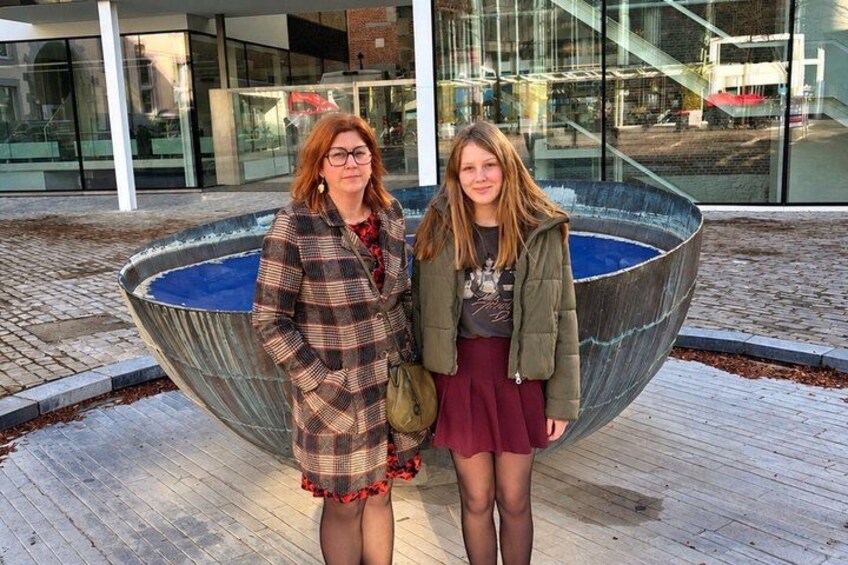 Twee personen staan voor een groot metalen sculptuur met een blauw interieur. 2
