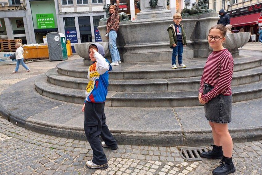 Een openbaar plein met een fontein, geplaveid met cobblestones, en mensen die lopen. 5