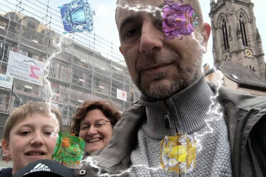 Una persona con un maglione grigio e una sciarpa colorata a motivi gialli e verdi, in piedi di fronte a un edificio con una torre dell'orologio. 4