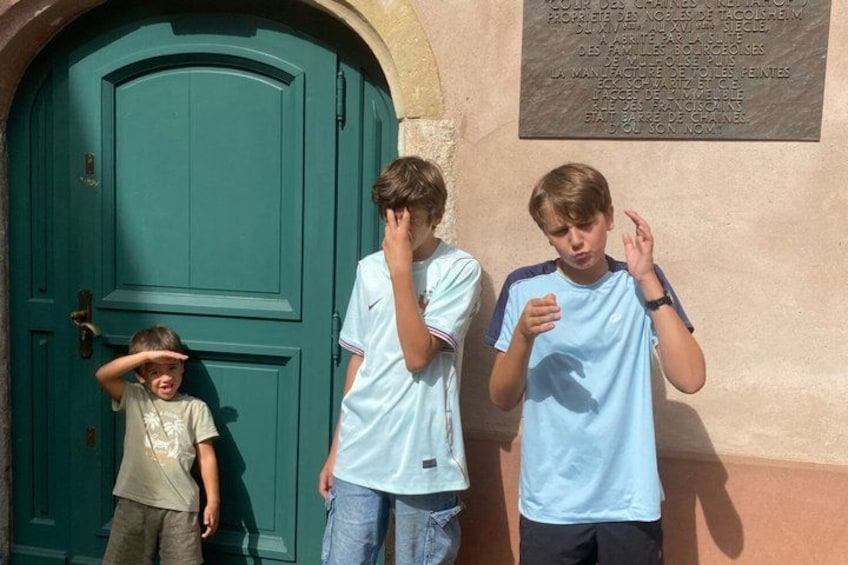 Tre bambini in piedi di fronte a una porta verde con una targa appesa al muro. 2