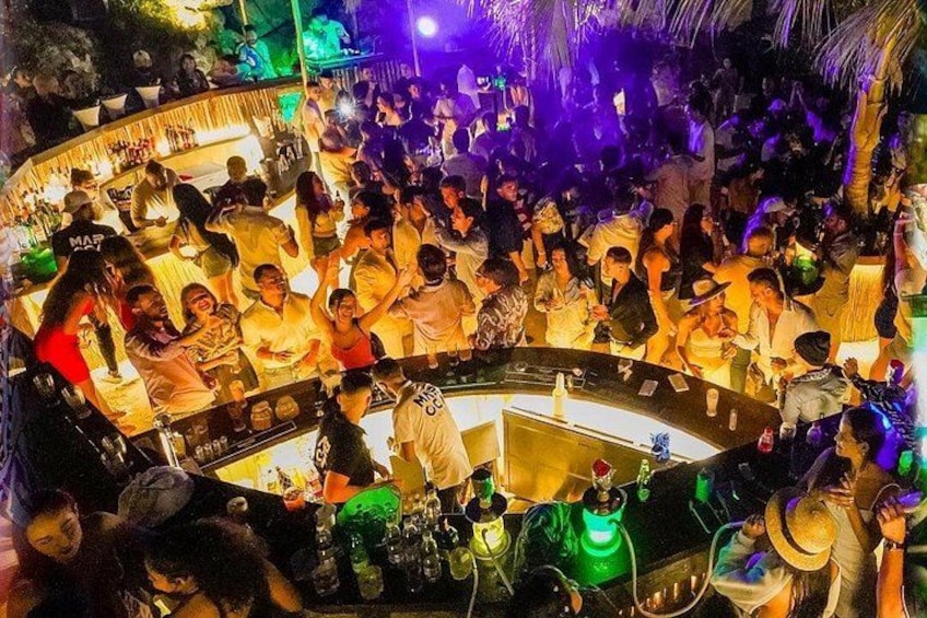 Een drukke bar met mensen die socialiseren en een DJ-podium in het midden. 4