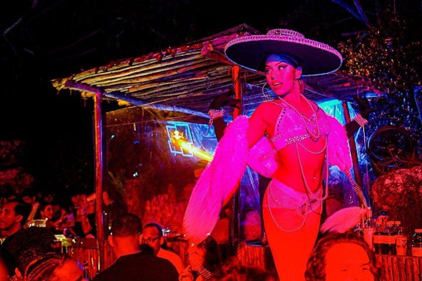 Een persoon in een levendig, kleurrijk kostuum met een grote sombrero, op een feestelijke locatie buiten, met een menigte op de achtergrond. 2