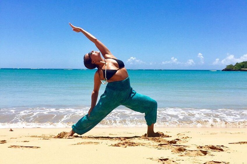A person performing a yoga pose on a beach with the ocean and a clear sky in the background. 3