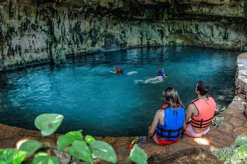 Two people observing kayakers in a clear blue pool with rocky walls. 1
