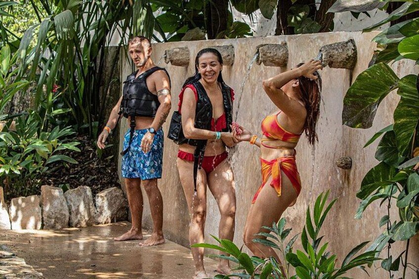 Three people in a tropical setting, one wearing a red swimsuit, another in a blue swimsuit, and the third in a black vest and shorts. 3
