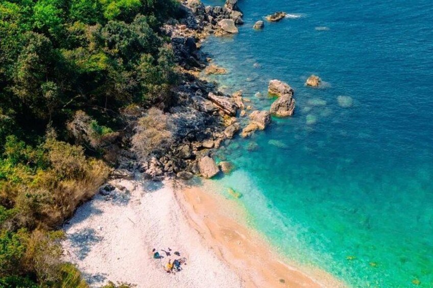 A coastal landscape with a sandy beach, clear turquoise waters, and rocky outcrops. 4