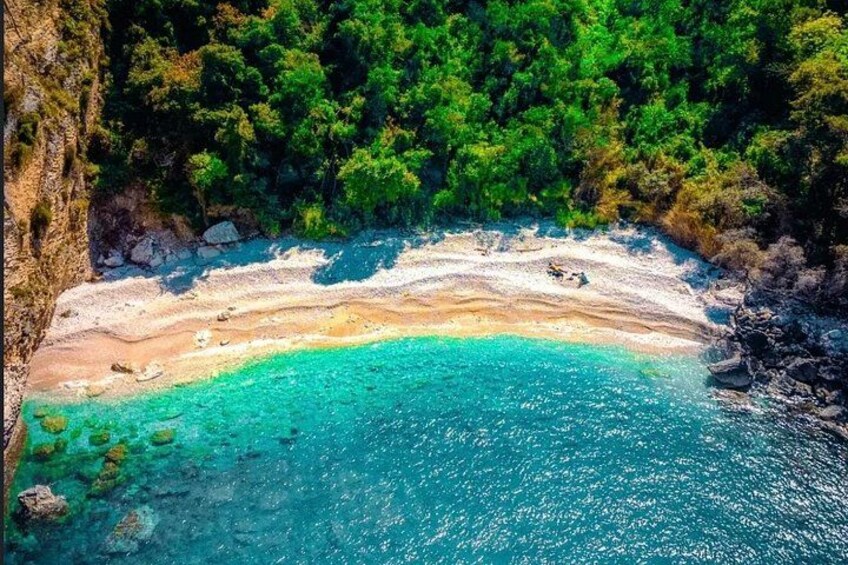 A coastal landscape with a sandy beach, clear turquoise waters, and dense green forest. 5