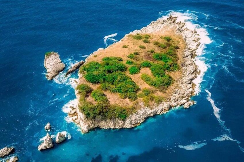An aerial view of a small island with rocky coastline, green vegetation, and clear blue waters. 2