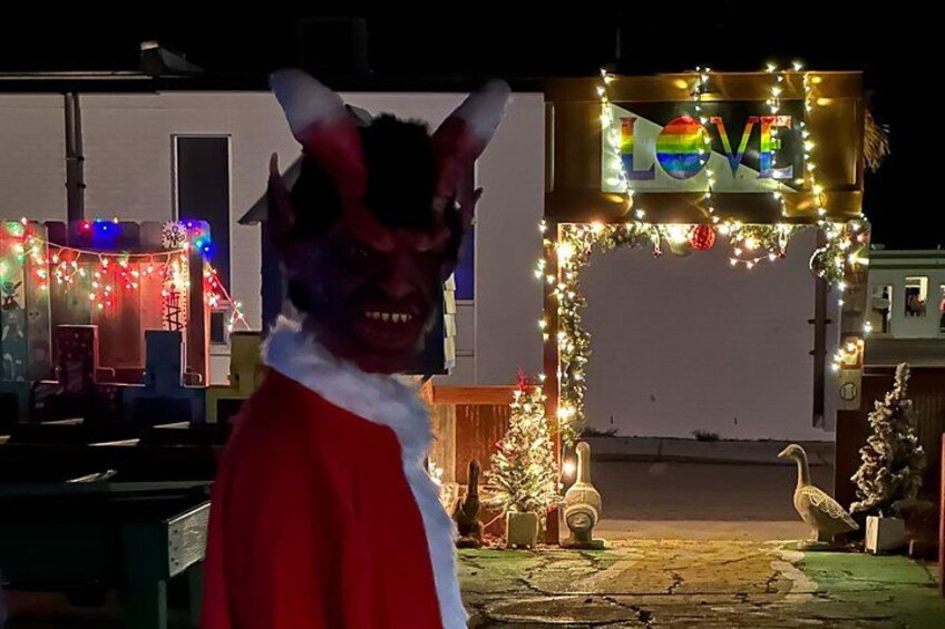 A person in a red and white costume with horns, standing in front of a decorated archway with the word 'LOVE' and lights. 4