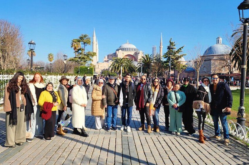 Un grupo de personas de pie sobre un camino empedrado, con un edificio histórico al fondo. 2