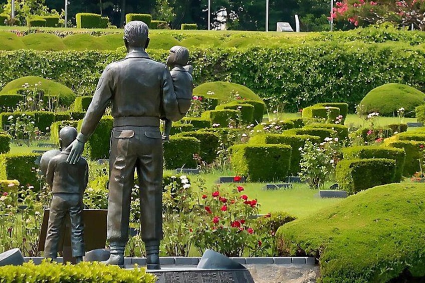 En staty som föreställer en man med ett barn, omgiven av välskötta häckar och blommor. 2