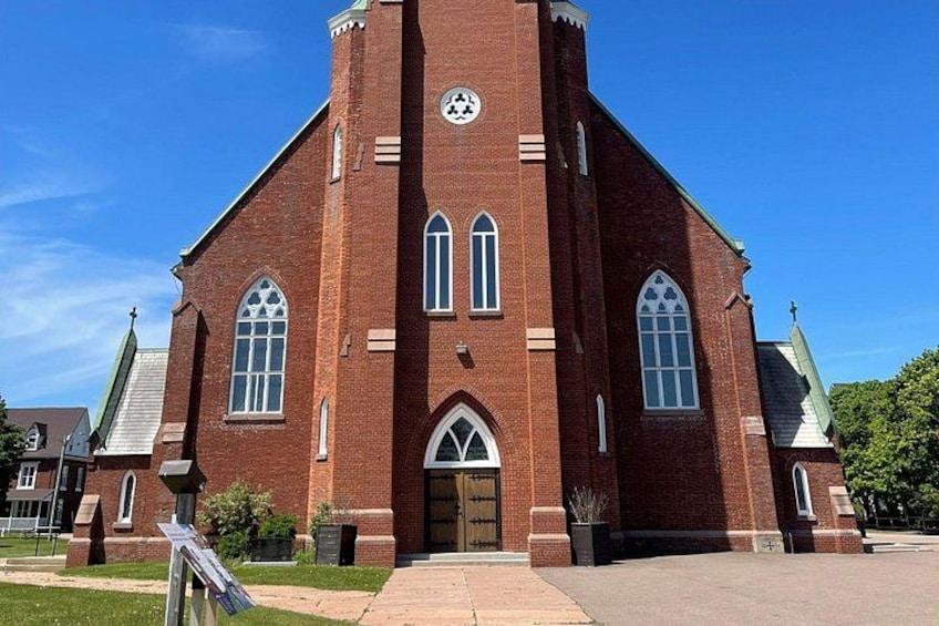 A red brick church with a tall steeple, arched windows, and a cross at the top. 1