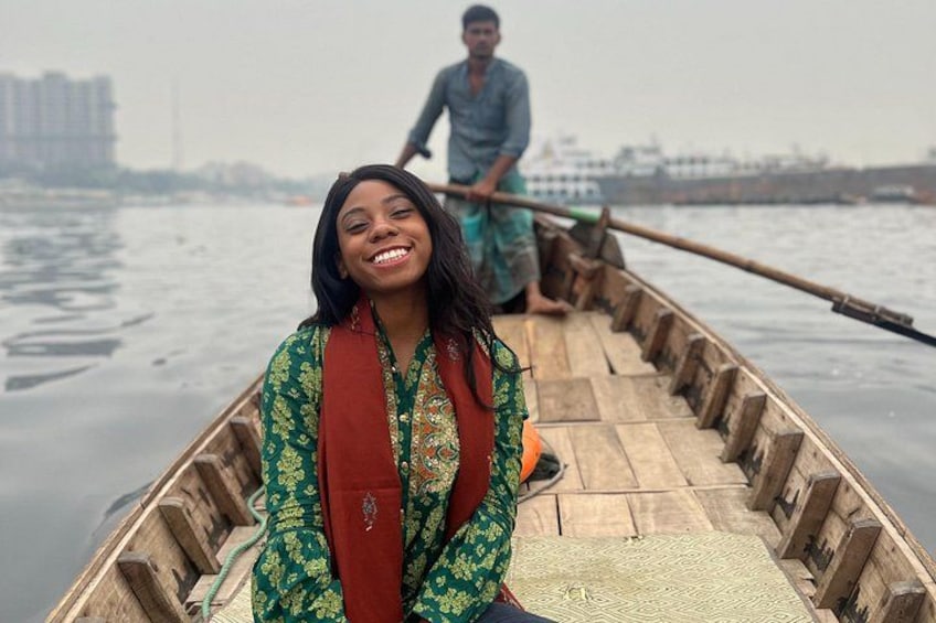 A wooden boat on water with a person in the foreground and another person rowing in the background. 1