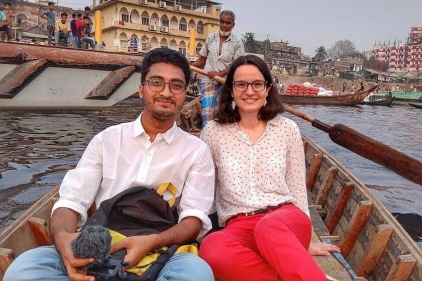 Two people in a wooden boat on a river with buildings in the background. 2