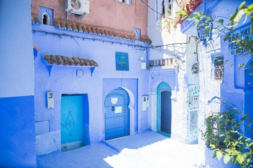 Een smalle steeg met blauw geschilderde gebouwen, een bord met de tekst 'Riad Yazid' en een betegeld dak. 3