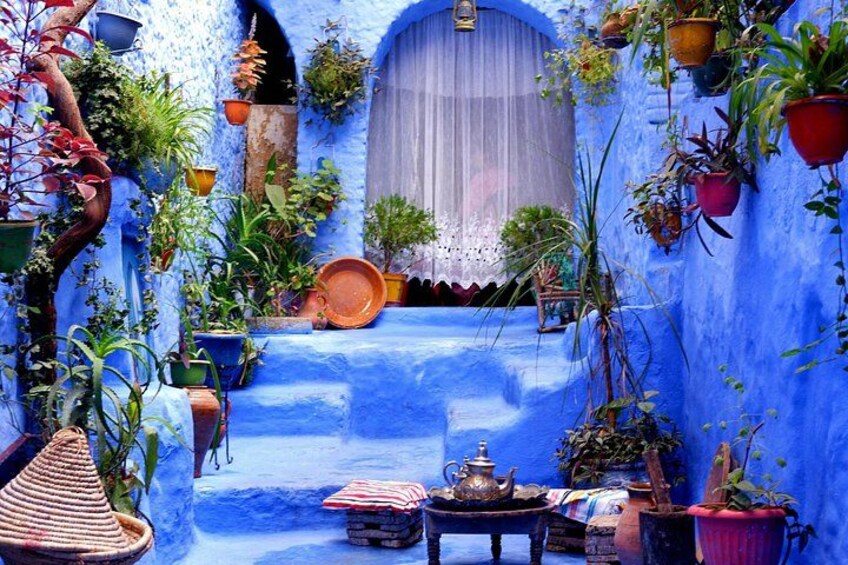 Een blauw betegelde binnenplaats met potplanten, een tafel met theepot en een traditionele Marokkaanse deur. 2