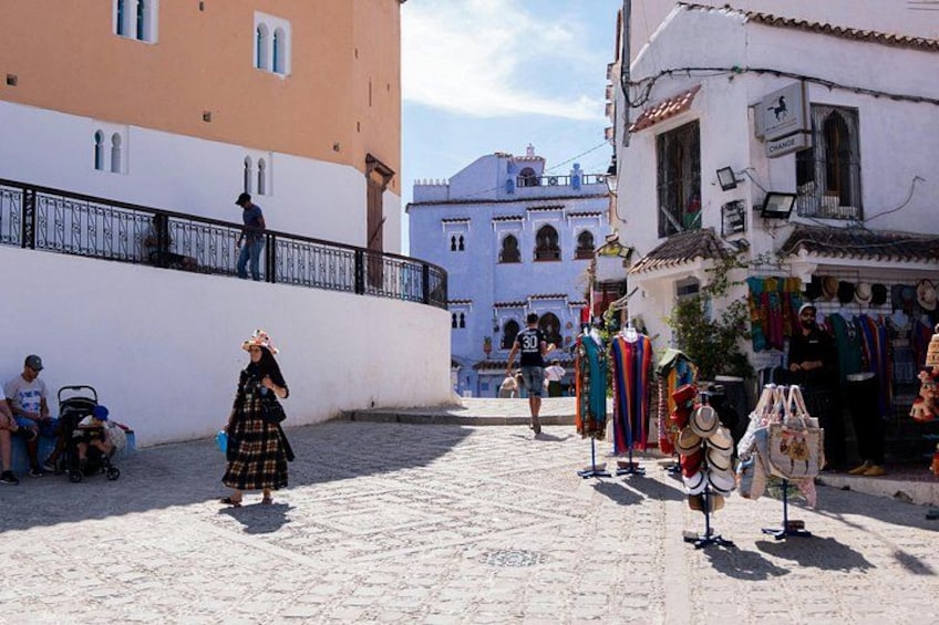 A cobblestone street with buildings, a woman in traditional dress, and a man on a balcony. 4