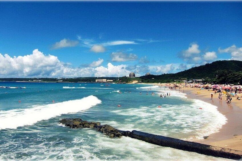 Una playa con olas, gente y una estructura en forma de cúpula a lo lejos. 2