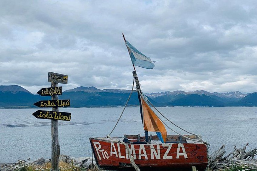 En båd ved navn 'P. ALMANZA' med et sejl, et skilt med flere vejskilte, og et bjergrigt landskab i baggrunden. 2