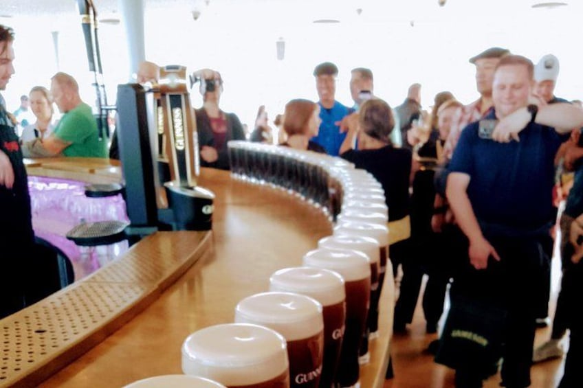 A bar with a long counter, glasses of beer, and people standing around. 4