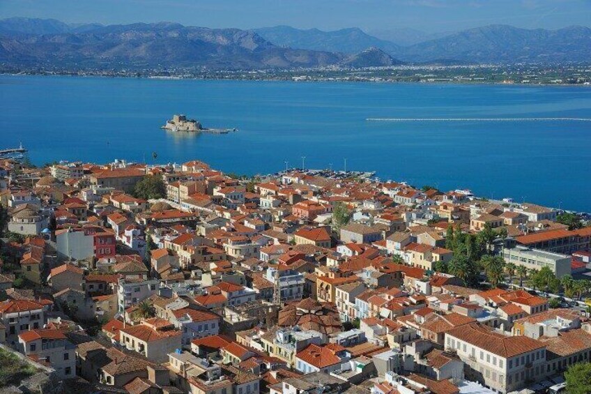 A coastal town with red-roofed buildings, a body of water, and distant mountains. 2