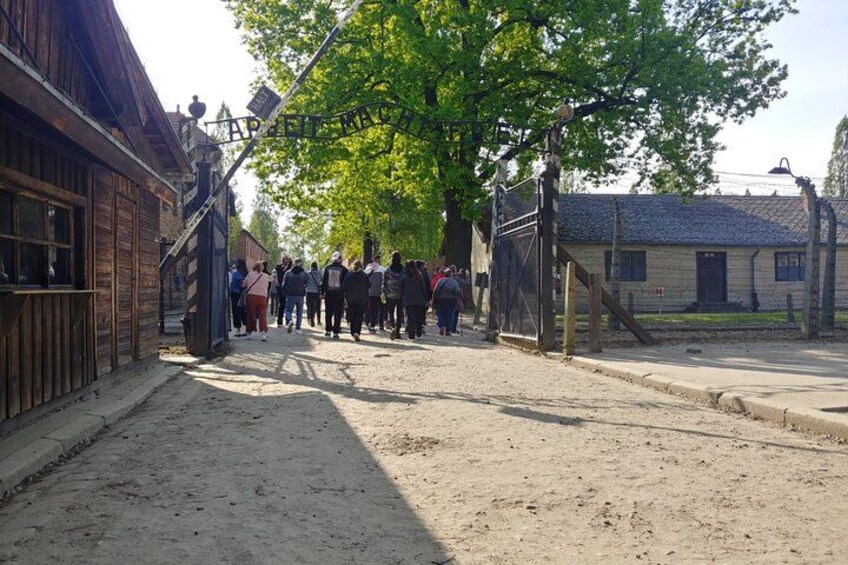 A dirt road with a group of people walking, wooden buildings, and a large tree. 2