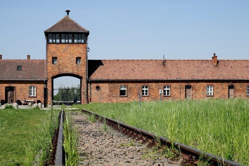 A brick building with a tower, a railway track, and a grassy field. 3