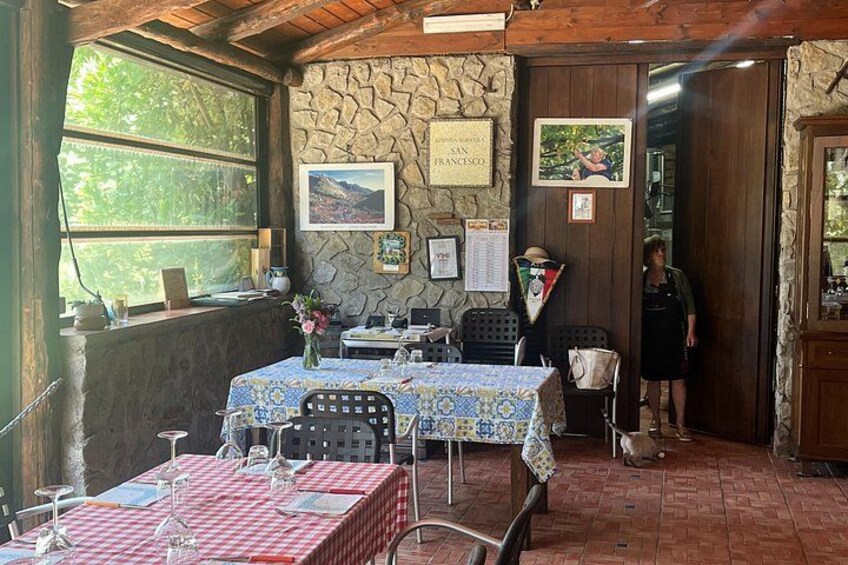 A rustic dining area with stone walls, a wooden ceiling, and tables set with tablecloths and glassware. 3