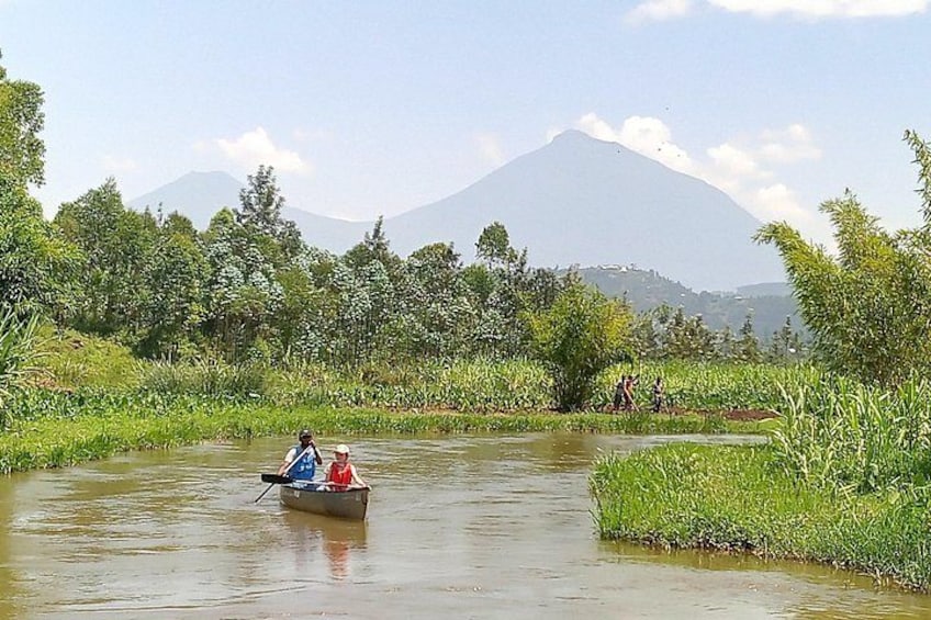 Un río con una barca que transporta a dos personas, rodeado de vegetación exuberante y una montaña al fondo. 5