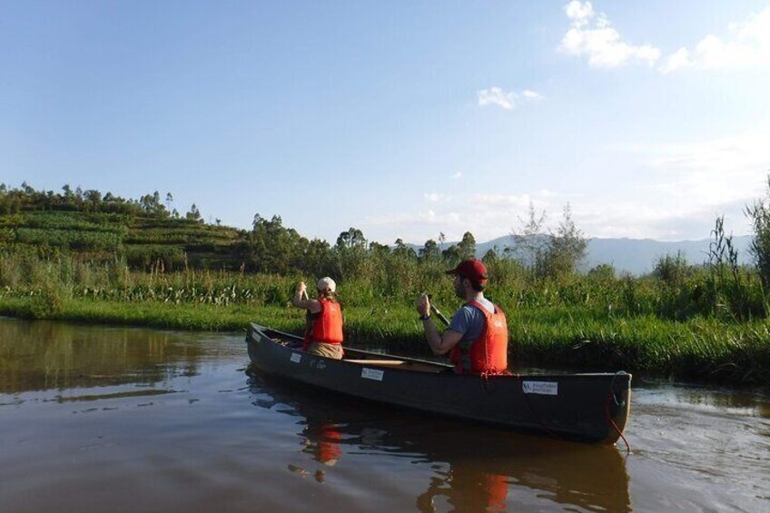 Due persone in una canoa su un fiume tranquillo, circondate da vegetazione rigogliosa e colline lontane. 3
