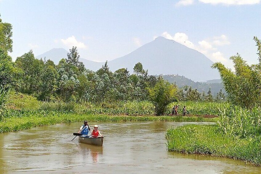 Un fiume con una barca che trasporta due persone, circondato da vegetazione lussureggiante e una montagna sullo sfondo. 5