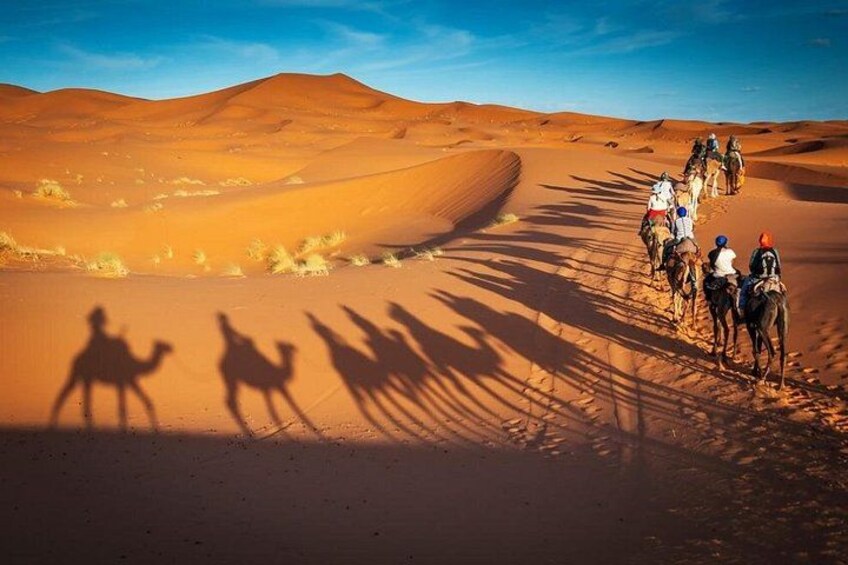 A group of people riding camels across a desert landscape with sand dunes. 2