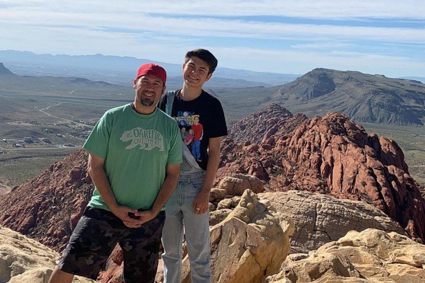 Two people standing on a rocky outcrop with a mountainous landscape in the background. 2